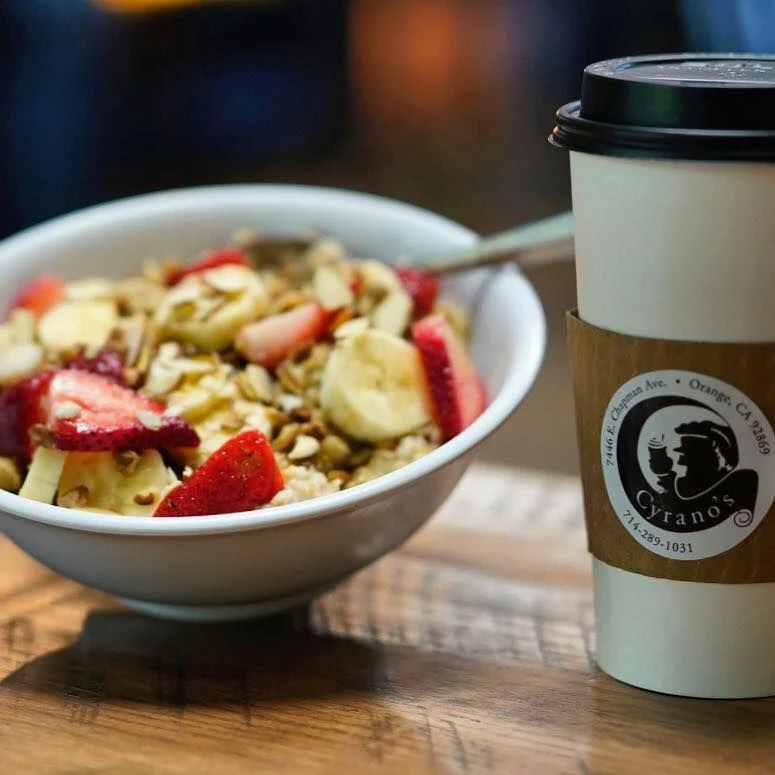 Oatmeal with strawberries beside a Cyrano's coffee